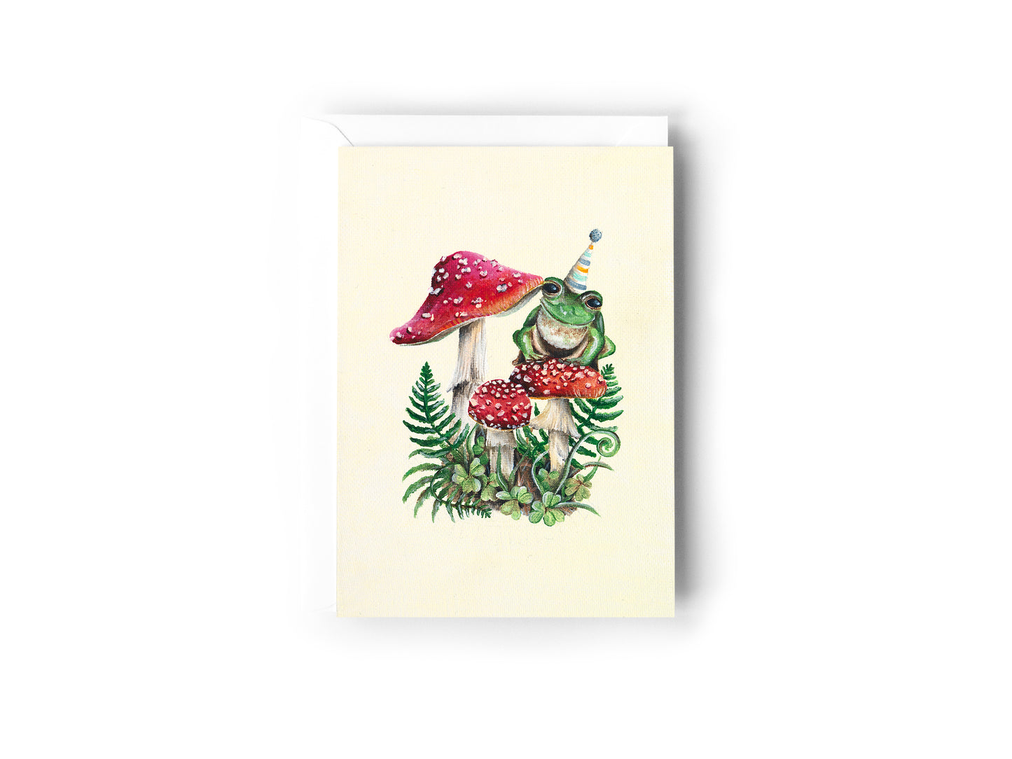 Cream birthday card with frog in a party hat sitting on red toadstools illustration.